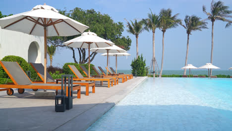 umbrella-with-bed-pool-around-swimming-pool-with-ocean-sea-background---holiday-and-vacation-concept