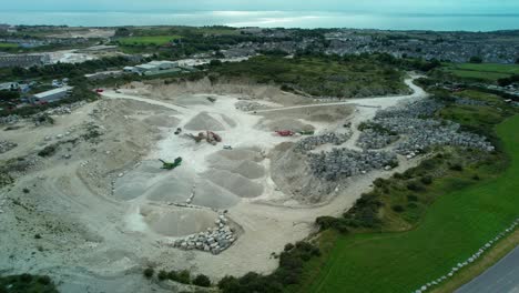 Massive-piles-of-gravel-and-stone-with-heavy-equipment-in-quarry,-aerial-orbit-view