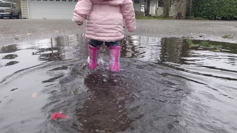 Walking-slowly-behind-a-little-girl-walking-through-a-puddle-wearing-pink-rubber-boots