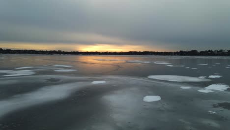 Aerial-view-of-a-frozen-lake-with-rare-ice-formations,-sun-setting-on-the-horizon