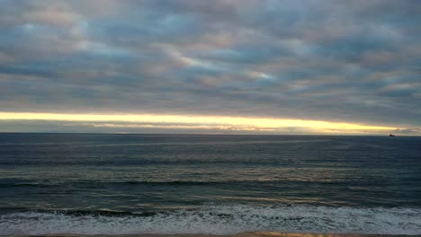 Meereswellen-Rollen-Am-Strand-Mit-Sonnenuntergangsfarben-Am-Horizont
