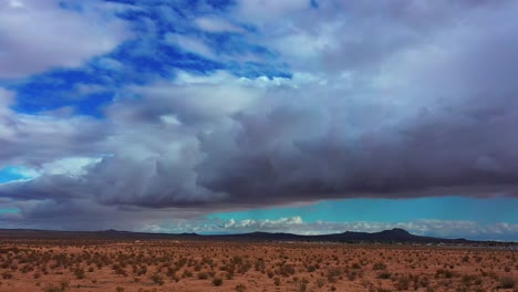 Cuenca-Del-Desierto-De-Mojave-Con-Las-Lejanas-Y-Escarpadas-Montañas-En-Un-Día-Nublado-Con-Grandes-Cúmulos-En-El-Cielo---Vista-Aérea-Deslizante