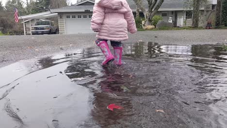 Close-up-of-a-little-girl-walking-through-a-large-puddle-wearing-pink-rubber-boots