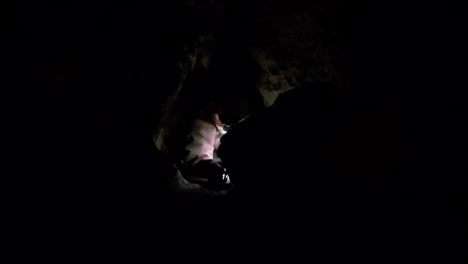 Expedition-caver-drags-gear-bag-down-dark-narrow-passage-in-blackness