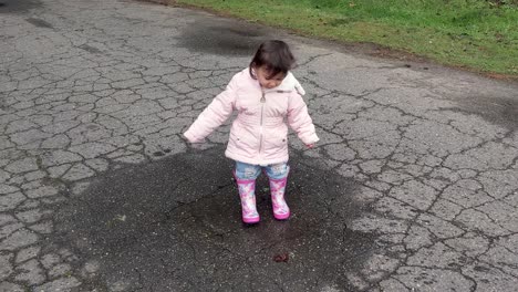 A-little-girl-is-so-excited-to-be-outside-and-jumping-in-tiny-puddles-in-pink-rubber-boots