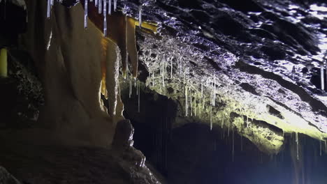 Yellow-stalactite-drips-water-onto-stalagmite-below-in-deep-dark-cave