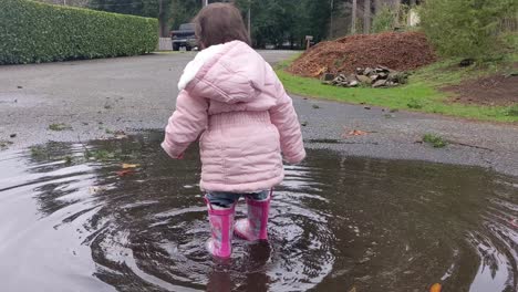 A-cute-little-girl-is-so-excited-to-be-in-a-large-puddle-wearing-pink-rubber-boots