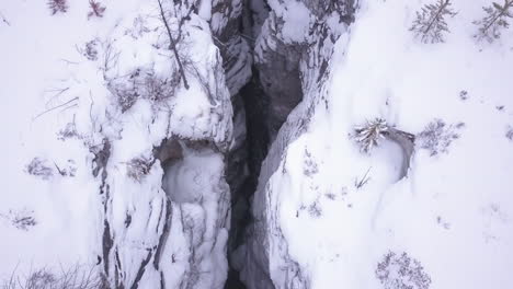 Aerial:-Deep-canyon-narrow-walls-hide-icy-river-far-below-in-winter