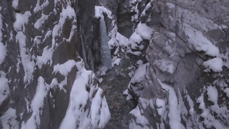 Icicle-aerial-rises-out-of-steep,-deep-narrow-rock-canyon-in-winter