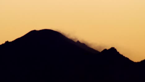 Macro-close-up-of-mountain-top-silhouette-at-sunset,-bird-flying