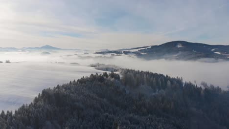 Incredible-drone-flight-over-snowy-winter-forest-landscape-with-clouds-and-mountains