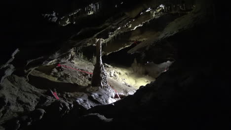 Unseen-caver-lights-calcite-column-in-muddy-underground-cave-chamber
