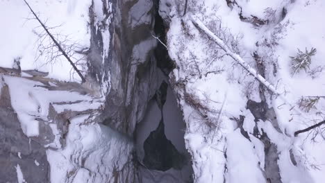 Vertical-aerial-of-narrow-winter-river-canyon-with-running-water-below
