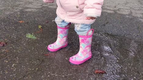 Close-up-of-a-little-girl-wearing-pink-rubber-boots-jumping-in-a-small-puddle
