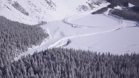 Cold-winter-aerial-descent-to-snowy-highway-loop-at-base-of-big-hill