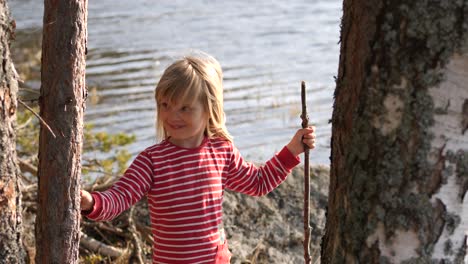 Beautiful-female-child-with-blonde-hair-enjoys-sunny-day-in-forestry-lakeside,-handheld-view