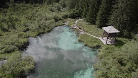Video-Mit-Drohnenansicht-Des-Vogels,-Der-Sich-Vom-See-Des-Flusses-Sava-Im-Naturschutzgebiet-Von-Zelenci-Mit-Touristen-In-Slowenien-Zurückzieht