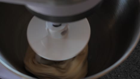Slow-motion-close-up-shot-of-dough-being-beaten-on-white-kitchen-aid-mixing-hook-in-large-silver-bowl