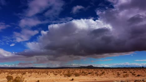 Mojave-Desert-with-stormy-rain-clouds-overhead-and-the-distant-mountains-in-silhouette---sliding-aerial-view