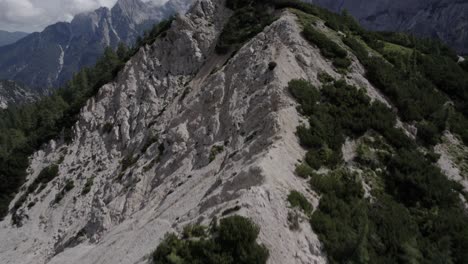 Drone-video-with-an-ascending-frontal-descriptive-plane-over-the-Vrsc-pass-in-Slovenia-with-hiker-at-the-top-ascending-walking-and-a-horizon-with-mountains