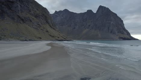 Aerial-drone-view-circling-low-over-tranquil-beach,-in-cloudy-Kvalvika,-in-Lofoten,-Norway