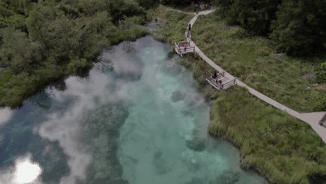 Beschreibendes-Frontales-Drohnenvideo-Des-Sava-Flusssees-Im-Naturschutzgebiet-Zelenci-Mit-Touristen-In-Slowenien
