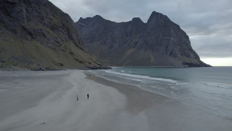 Aerial-view-of-people-walking-on-the-Kvalvika-beach,-in-cloudy-Lofoten,-Norway---tracking,-drone-shot