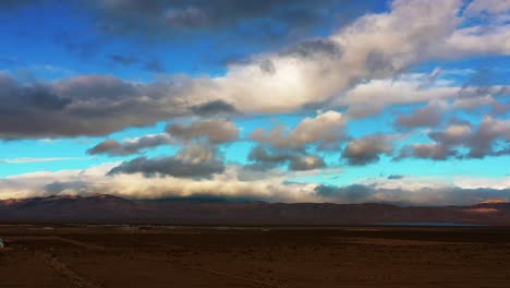 The-Mojave-Desert-basin,-a-distant-mountain-range-and-lake-with-clouds-and-blue-sky-above-at-sunset---aerial-view
