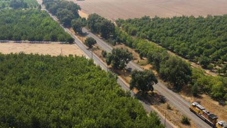 Drone-descent-while-passing-a-freight-train-next-to-a-farm-with-fruit-trees