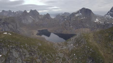 Aerial-view-over-mountains,-revealing-the-Reinefjord-in-Lofotodden-Nasjonalpark,-in-cloudy-Lofoten---pan,-drone-shot