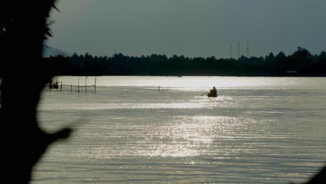 Eine-Abstrakte-Silhouettenaufnahme-Eines-Lokalen-Thailändischen-Fischers,-Der-Ein-Boot-In-Richtung-Des-Ufers-Des-Chanthaburi-flusses-Paddelt,-In-Der-Ferne-Der-Wunderschöne-Morgendliche-Sonnenaufgang,-Der-Vom-Wasser-Reflektiert-Wird,-Thailand