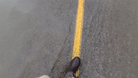 Walking-on-flooded-asphalt-road-with-yellow-line-in-middle,-POV-view