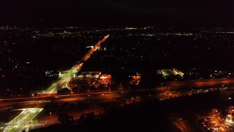 Slow-tracking-shot-of-cars-moving-along-highway-connection-below-at-night