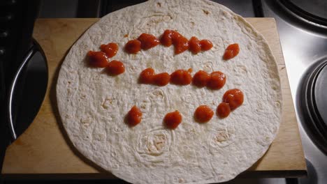 A-close-up-shot-of-a-tasty-tomato-sauce-strategically-being-dripped-onto-a-round-wheat-flour-wrap,-the-source-providing-the-base-layer-of-flavour-for-a-delicious-Hot-Dog-tortilla