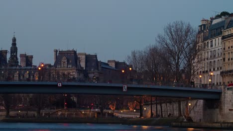 Tourists-crossing-river-seine-on-bridge-while-city-lights-light-up-Paris-time-lapse-4k-30p