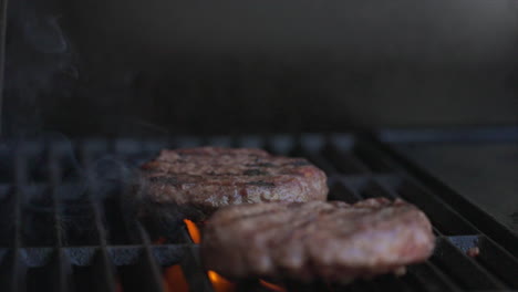 Slow-Motion-Close-Up-shot-of-two-burger-patties-sizzling-on-a-BBQ-as-orange-flames-shoot-up-from-below