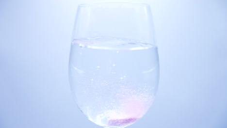 Zeitlupenaufnahme-Einer-Violetten-Vitamintablette,-Die-In-Ein-Glas-Wasser-Fällt-Und-Sich-Auflöst,-Um-Das-Wasser-Violett-Zu-Färben