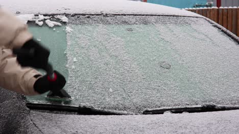 Man-In-Coat-And-Gloves-Cleaning-Frozen-Car-Windshield,-Scrapes-Ice-Off-The-Glass-Surface-In-Winter