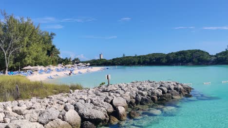 Eine-Paradiesische-Bucht-Mit-Felsen-Und-Sandstrand,-Sonnenschirmen-Und-Liegen-Auf-Der-Blauen-Laguneninsel,-Den-Bahamas