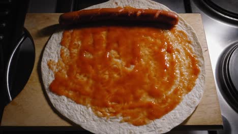 A-close-up-top-down-shot-of-a-hot-frankfurter-sausage-being-placed-onto-a-wheat-tortilla,-the-wrap-completely-covered-in-a-tomato-source-base-which-creates-an-amazingly-tasty-Tortilla-Hot-dog-meal