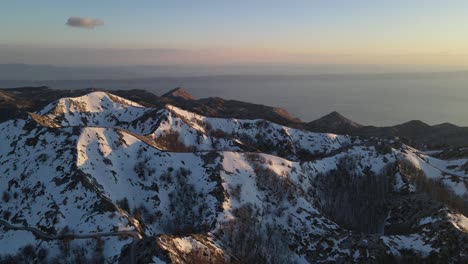 Snowy-mountains-against-sunset-sky-and-Adriatic-Sea,-Sveti-Jure,-Biokovo,-Croatia---Aerial-forward