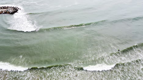 Eine-Vertikale-Aufnahme-Der-Wellen,-Die-Auf-Das-Ufer-Des-Sea-Links-Beach-Treffen,-Während-Ein-Paar-Surfer-Auf-Dem-Wasser-Herumhängen
