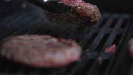 Slow-motion-close-up-shot-of-a-burger-patty-being-turned-over-on-a-BBQ-whilst-orange-flames-shoot-up-from-below