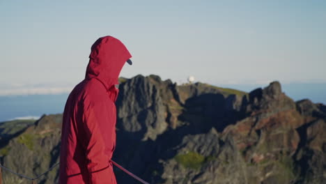 Person-in-red-jacket-looking-out-over-mountains-with-observatory-in-distance
