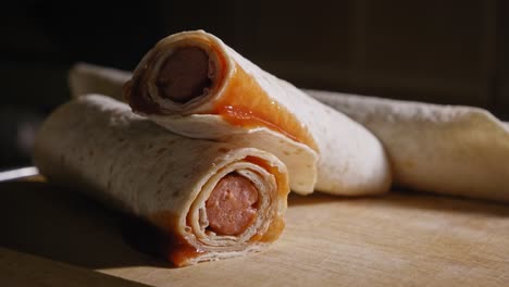 A-close-up-shot-of-a-complete-Tortilla-Hotdog,-a-grilled-frankfurter-sausage-wrapped-in-a-wheat-tortilla-neatly-presented-on-a-wooden-cutting-board