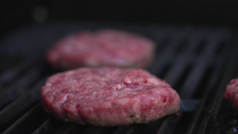 Pull-focus-close-up-shot-between-two-burger-patties-sizzling-on-a-BBQ