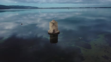 Old-Spanish-Mill-in-the-lagoon-at-the-island-town-Orbetello-close-to-Monte-Argentario-and-the-Maremma-Park-in-Tuscany,-Italy,-with-blue-sky-and-calm-blue-water