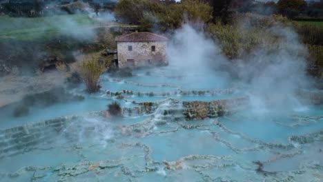 Flying-through-fog-at-the-thermal-hot-springs-bath-and-waterfall-at-Saturnia,-Tuscany-Italy-close-to-Siena-and-Grosseto