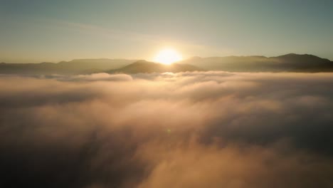Drone-Aerial-View-Flying-Above-Beautiful-Heavenly-Clouds-During-Epic-Warm-Sunrise-With-Mountains-In-Background