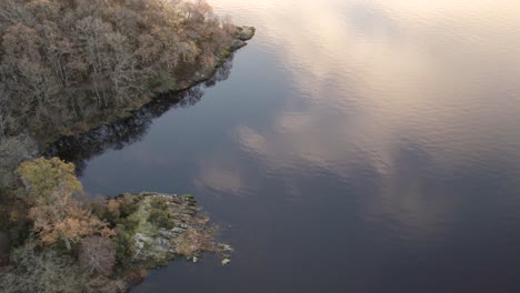 Luftdrohnenaufnahmen-Eines-Herbstsonnenaufgangs-Mit-Wolken,-Die-Sich-Im-Loch-Lomond-Spiegeln,-Mit-Einem-Boot,-Fliegenden-Vögeln-Und-Laubwäldern,-Die-Seine-Ufer-Im-Loch-Lomond-Und-Im-Trossachs-Nationalpark-Umarmen